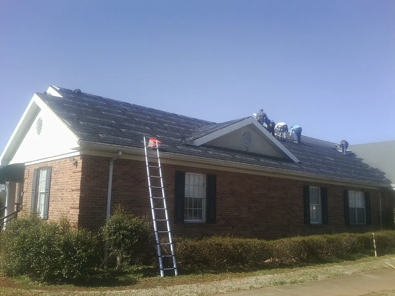 Crew tearing shingles off a brick ranch roof with a ladder set — Metal Roof Repair work by our crew in Yorkville